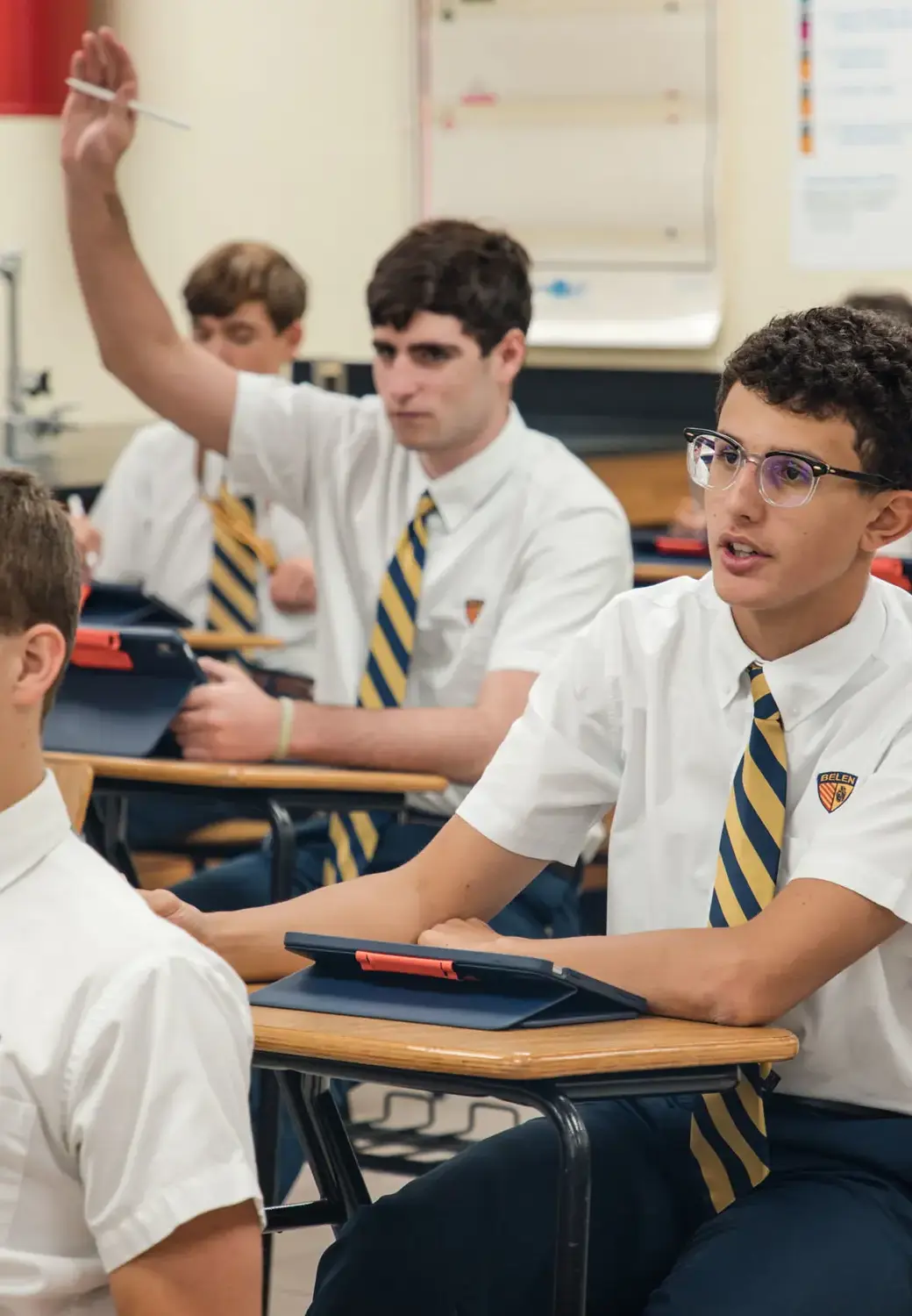 Belen Jesuit students with their hands up in class.