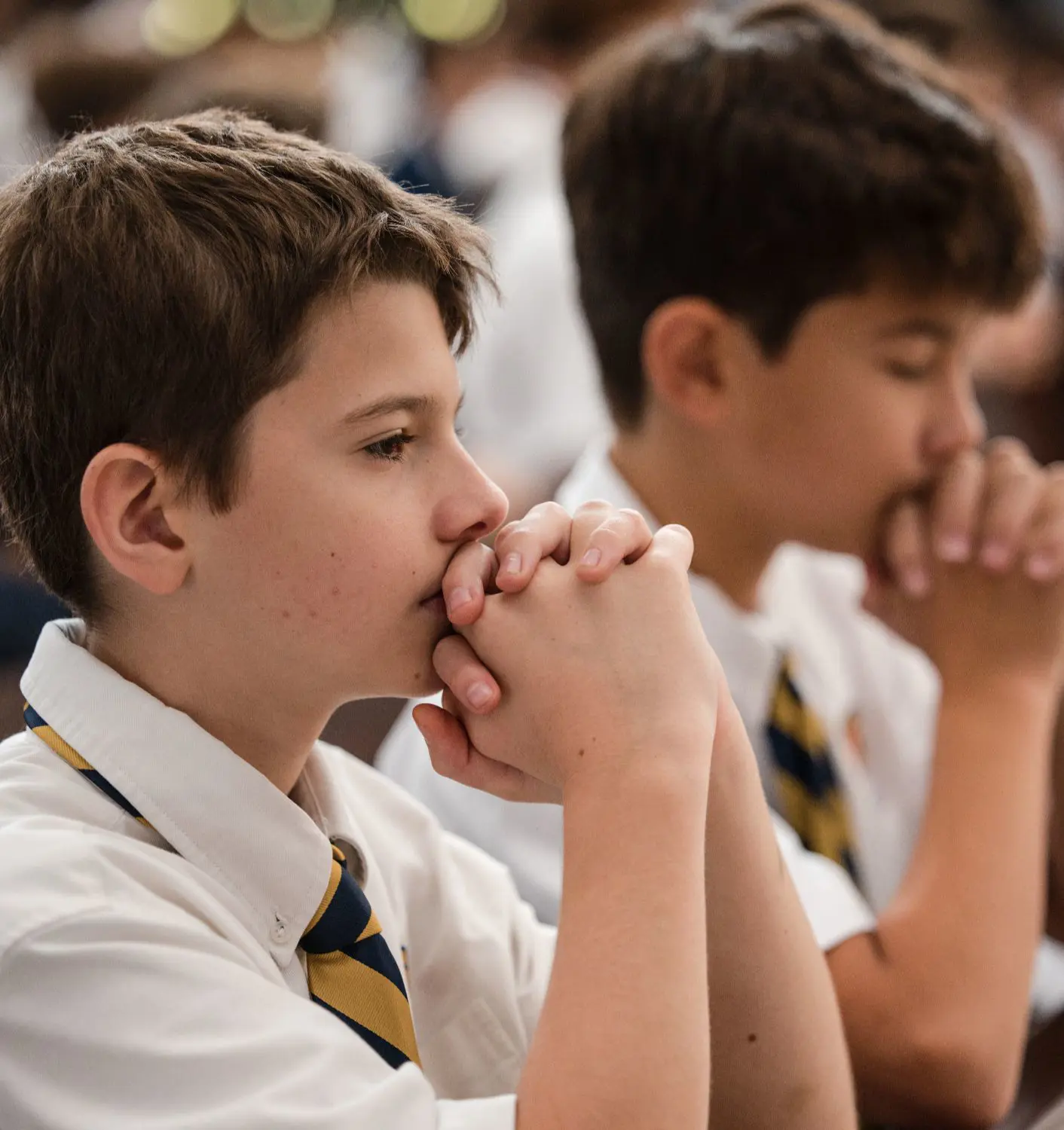 Two Belen Jesuit students in uniform are kneeling in prayer inside the Our Lady of Belen Chapel during a grade-level FLEX Mass.