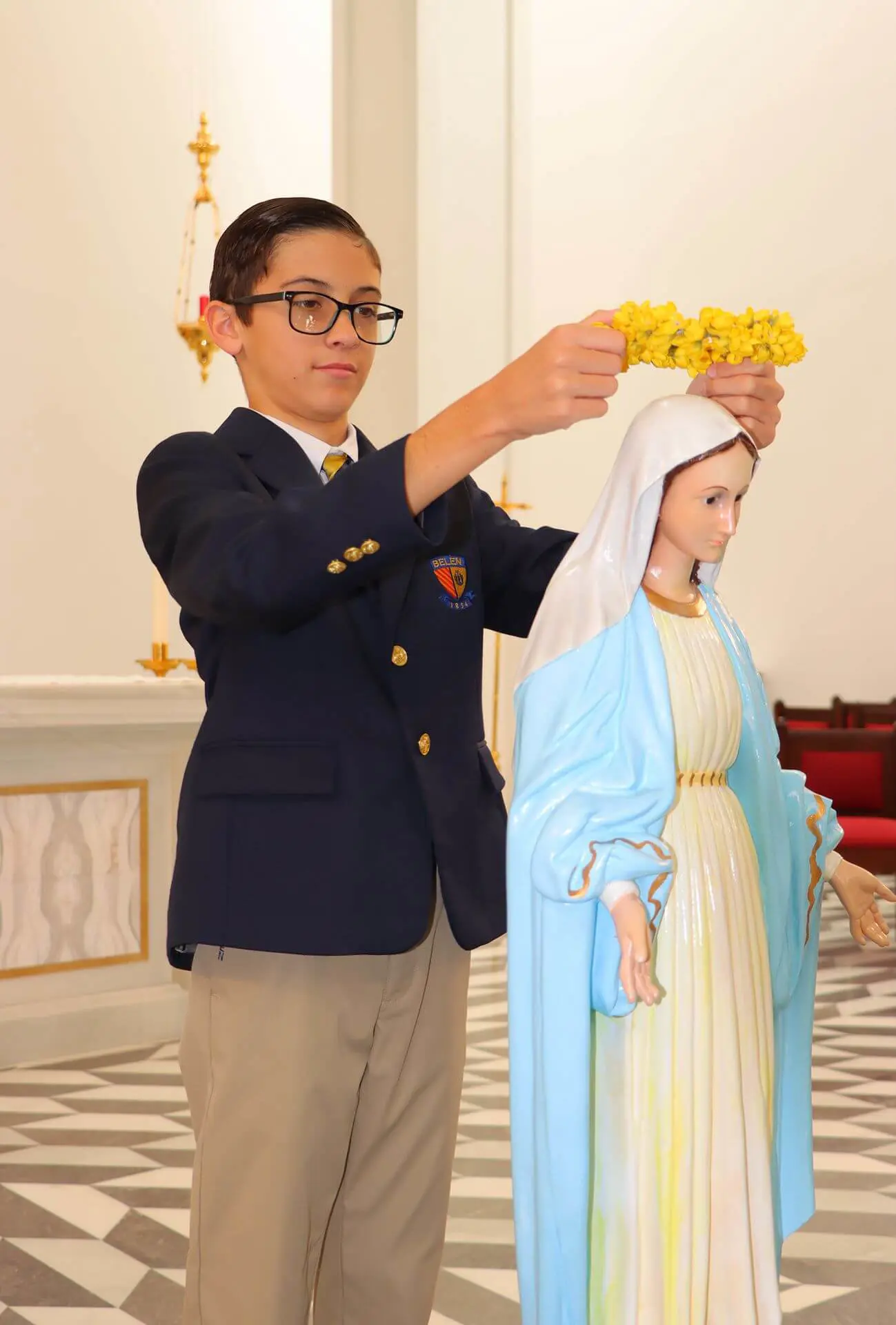 A Belen Jesuit Middle School student crowns the statue of Mary in the Our Lady of Belen Chapel. The crown is made of yellow flowers.