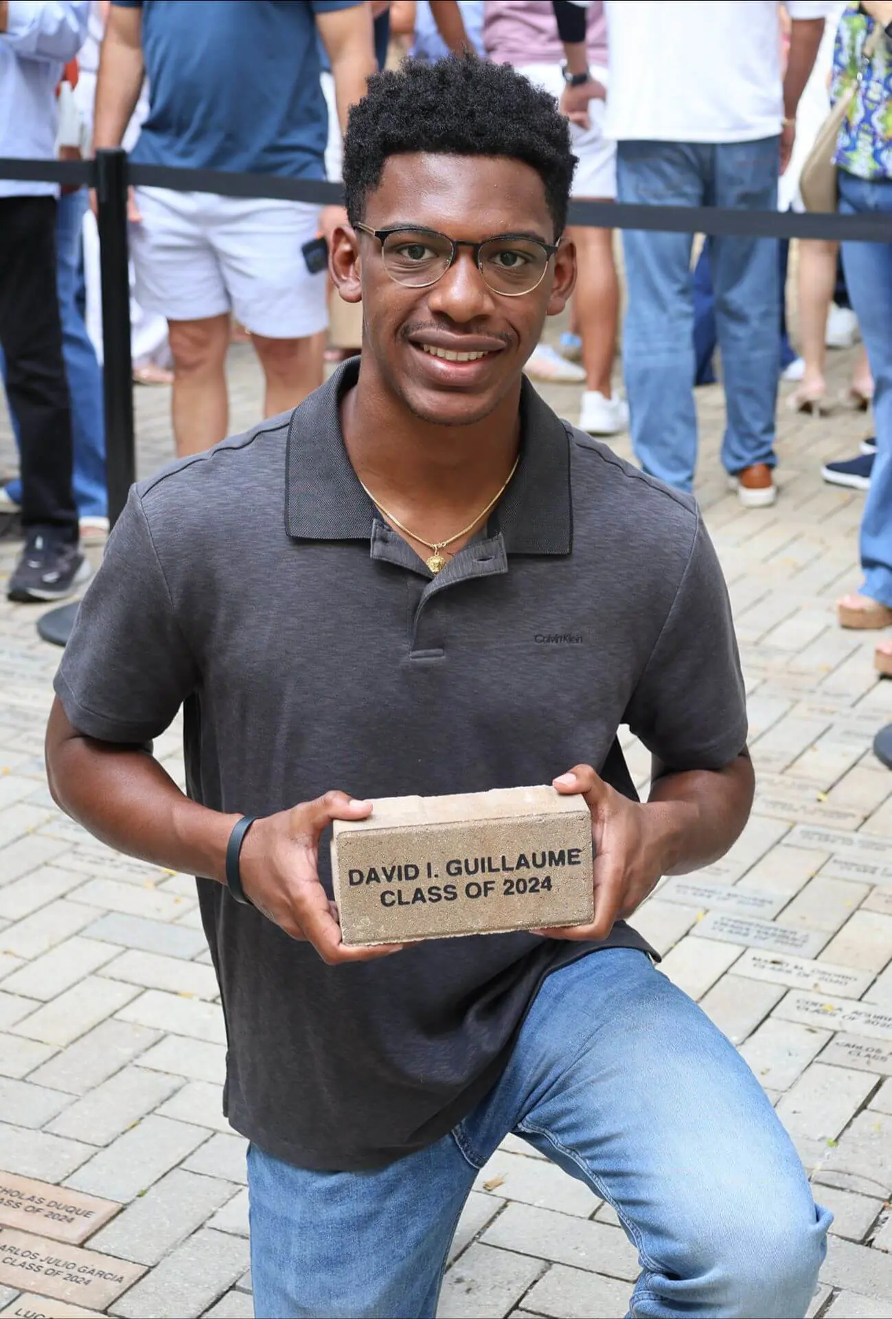 Belen alumnus David Guillaume from the class of 2025 takes part in the brick laying ceremony with his classmates. He is posed on a knee holding his brick before it is positioned in place.
