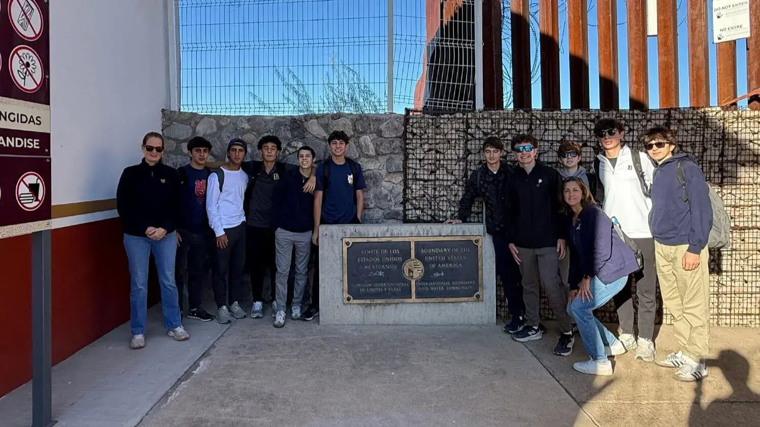 Belen Jesuit students who attended the 2025 Kinot Border Initiative Mission trip pose at a marker indicating the border of the United States and Mexico. 