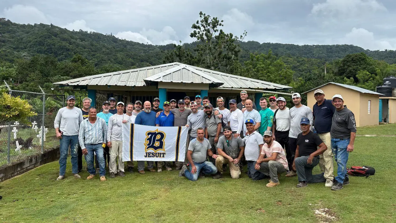 Belen Alumni on the 2025 mission trip to the Dominican Republic pose together, holding the Belen flag. Beautiful mountains and landscapes are in the background.