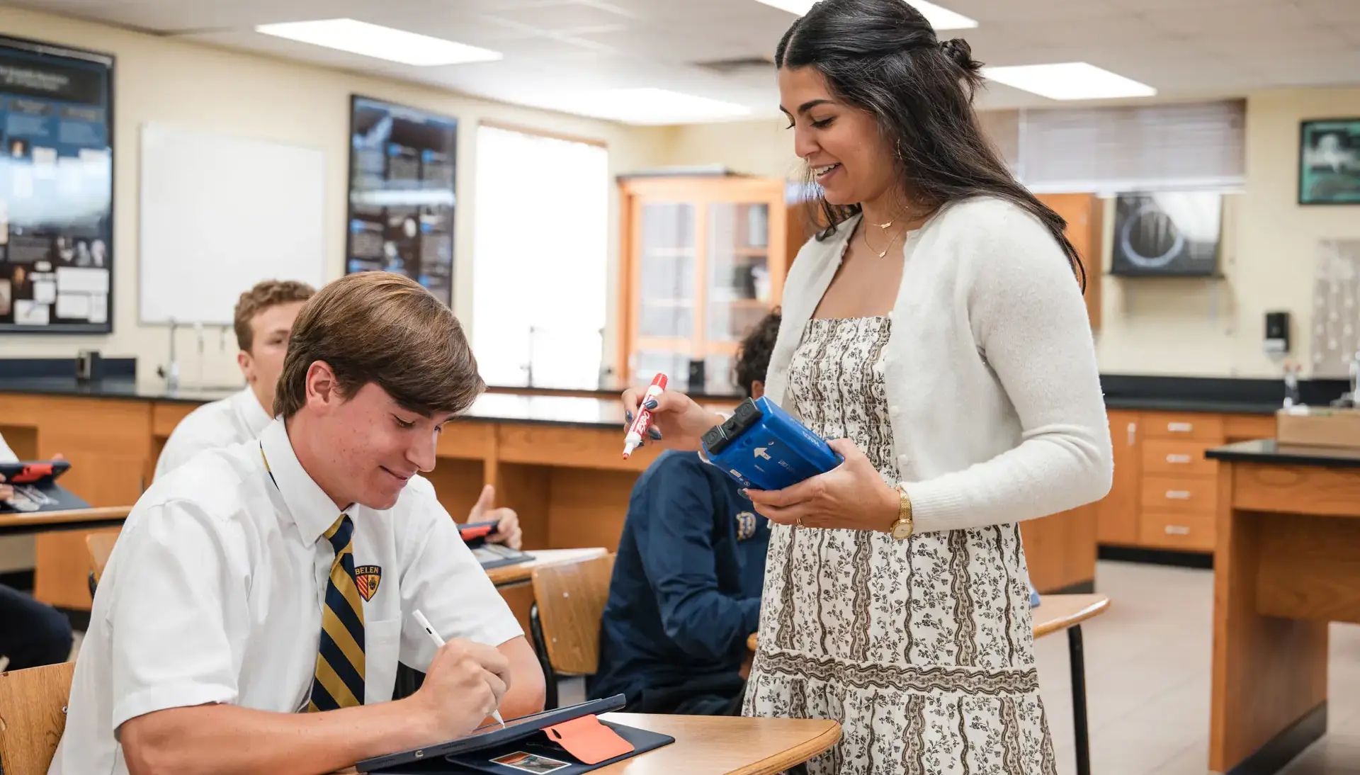 Belen Jesuit teacher Elizabeth De La Heria is pictured in her AP Physics 1 class assisting a student. High school students are seated at desks in a lab located in the Raúl and Nidia Rodríguez Science 