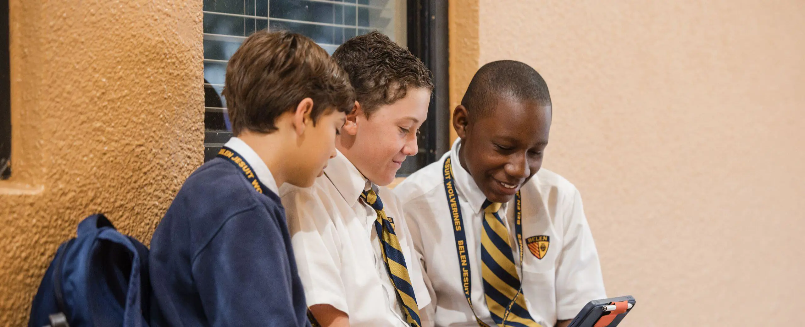 Belen Jesuit students sitting on a bench together using a tablet to complete class work.