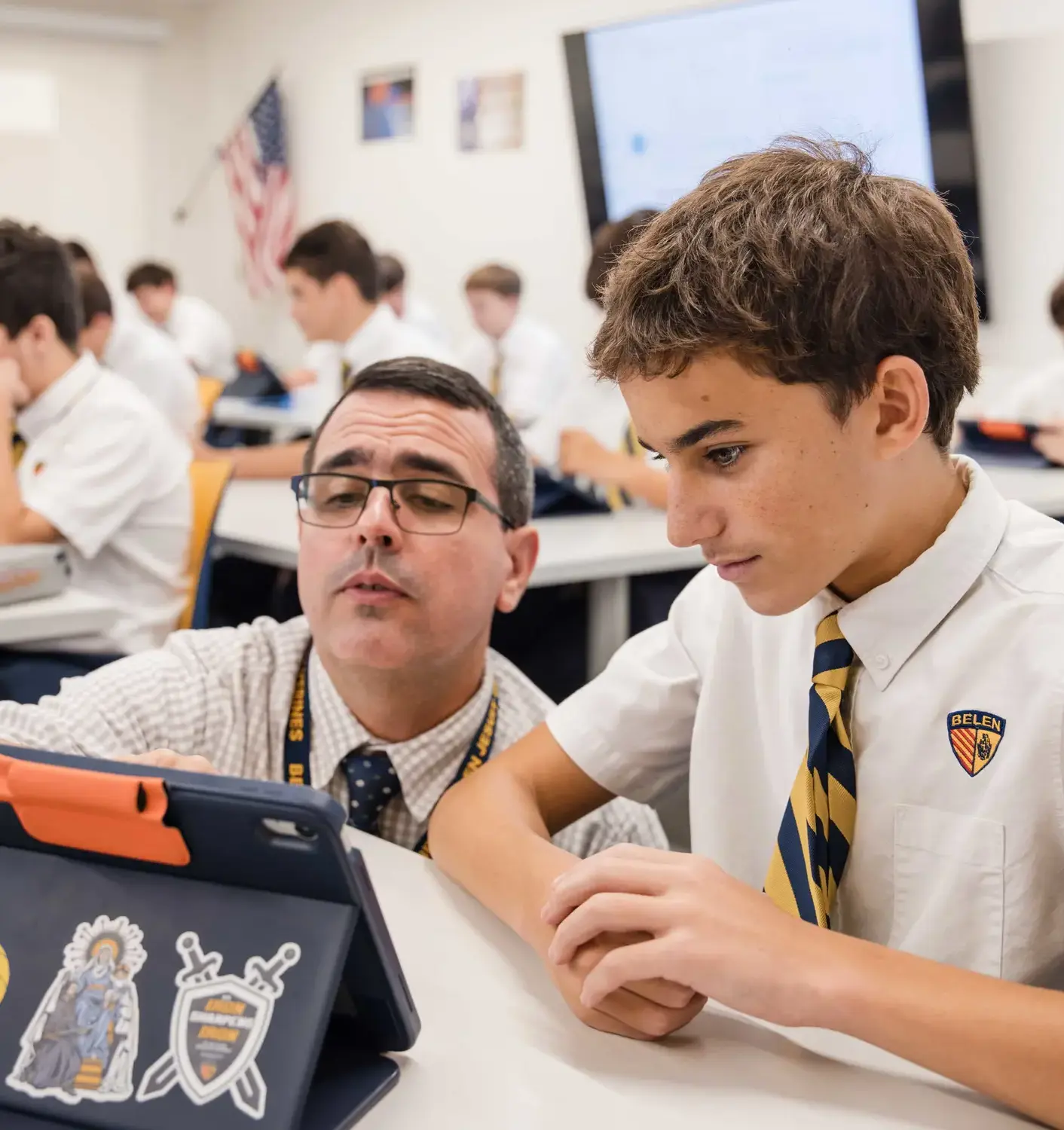 Geometry teacher Lazaro Suarez assists a Belen Jesuit student at his desk during class. The student is listening intently to the guidance.