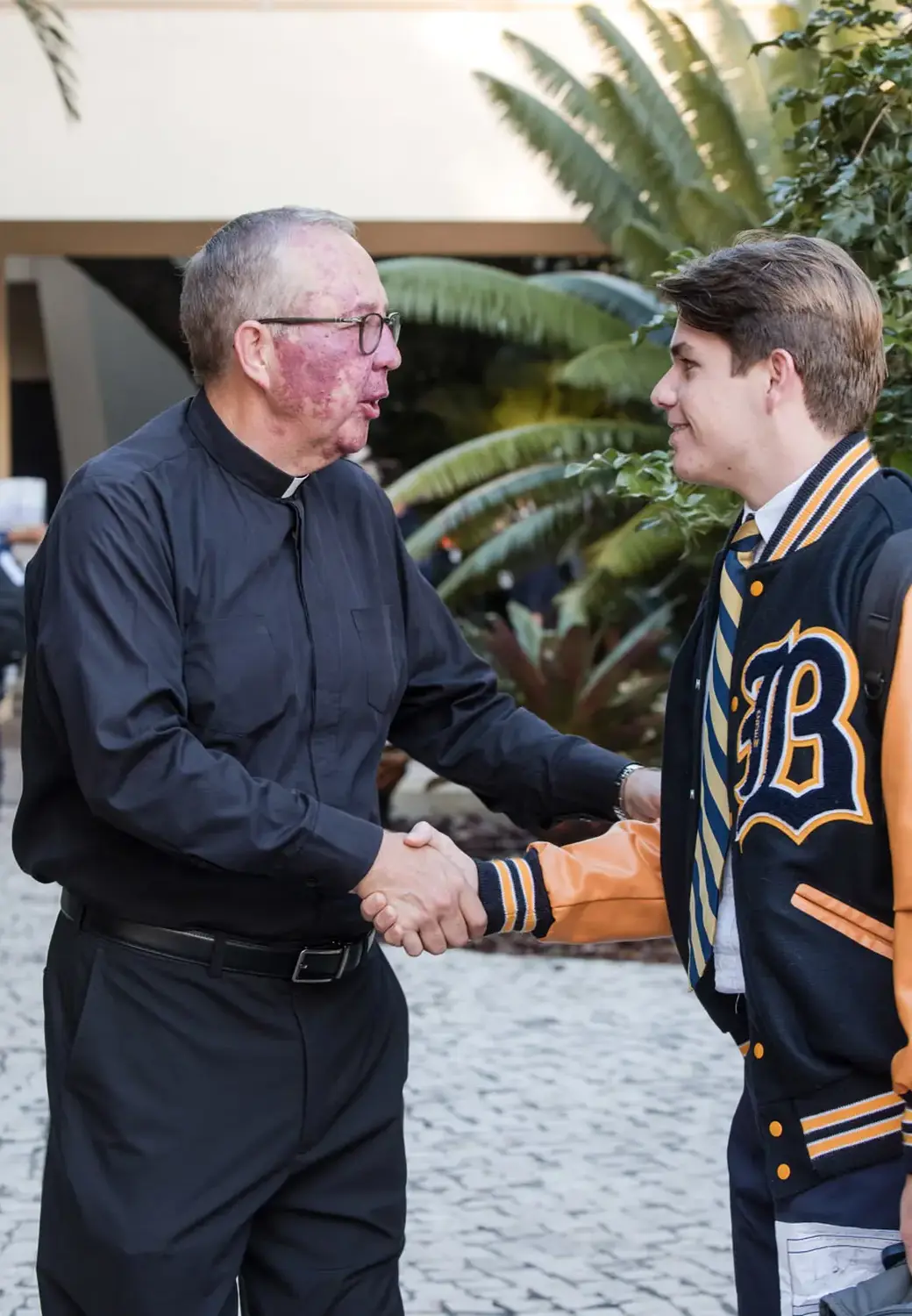 Belen Jesuit President shaking hands with a student wearing a wolverines jacket.