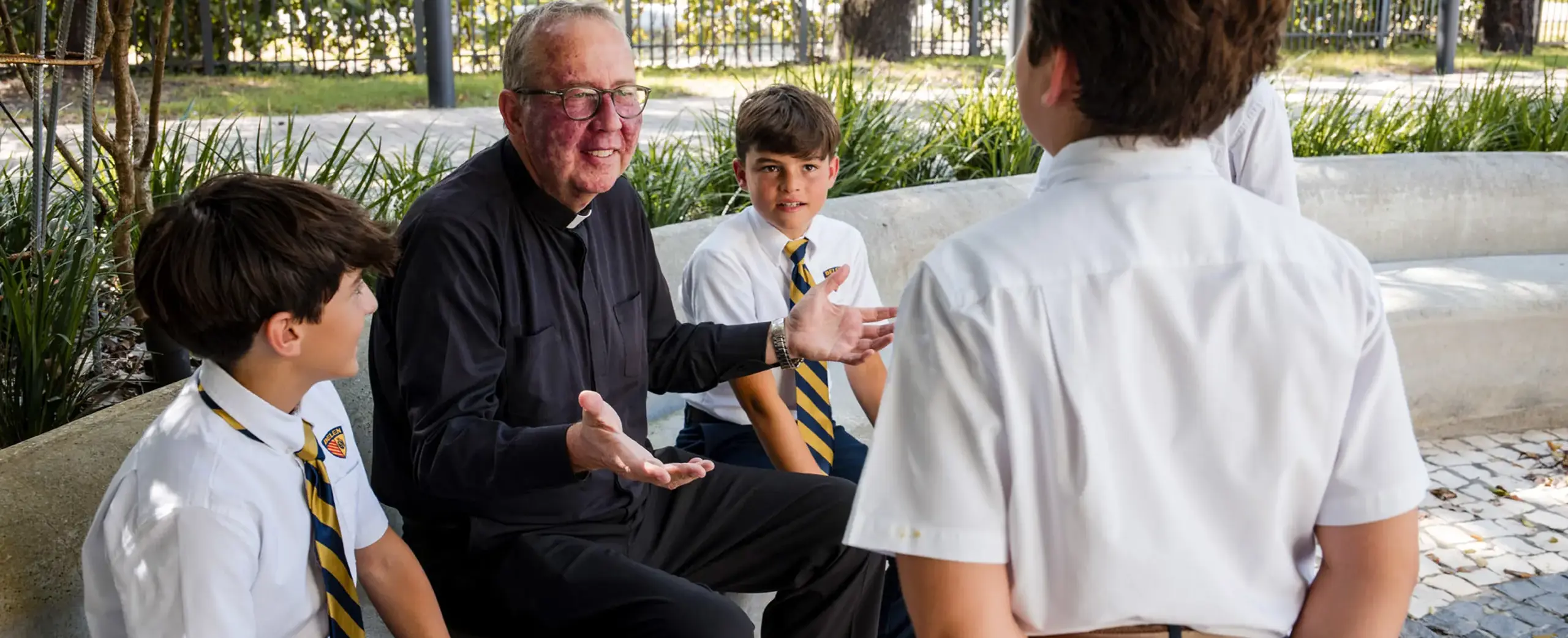Belen Jesuit President talking to a group of students on a bench outside.