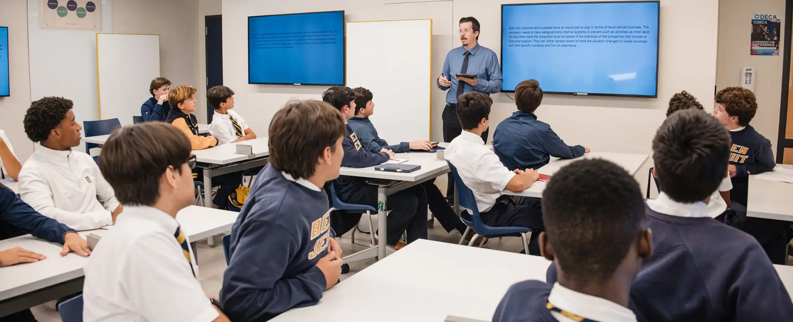 Belen Jesuit teacher Matthew Bowen is pictured leading his Principles of Business class. High school students are seated at desks, engaged in a lesson in a modern classroom.