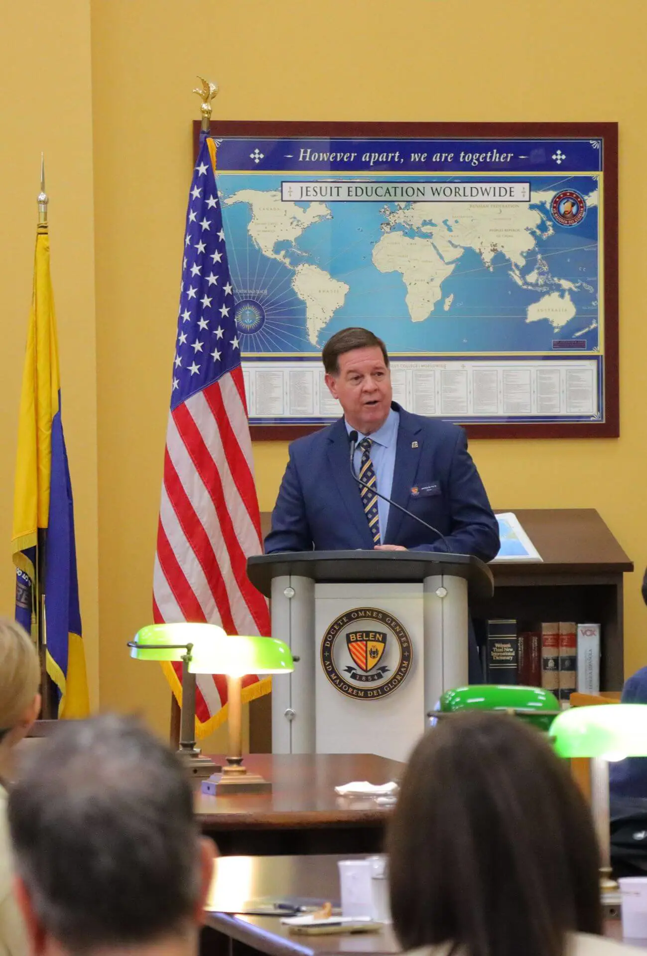 Belen Jesuit Principal Jose E. Roca ('84) speaking at a podium in the school's library, addressing an audience of parents.